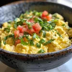A close-up side view of fluffy high-protein scrambled eggs garnished with fresh herbs.