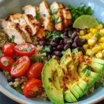 A vibrant avocado chicken quinoa bowl topped with cherry tomatoes and fresh cilantro.