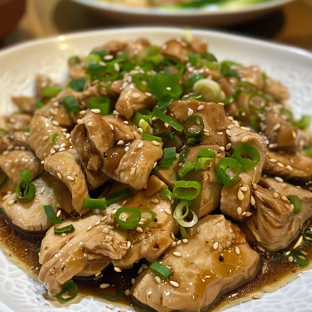 Close-up of tender, glazed chicken thighs infused with ginger slices and vibrant spring onions.