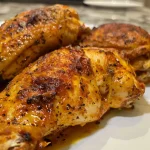 Juicy paprika chicken quarters displayed on a rustic wooden surface.