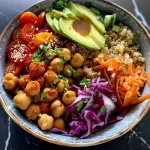 A vibrant chickpea bowl filled with fresh vegetables and grains, featuring avocado and tahini dressing.