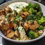 Close-up of grilled chicken and broccoli in a bowl with creamy sauce.