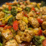 A side view of a colorful chicken and vegetable stir fry in a bowl.