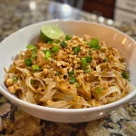 Close-up view of Thai Chicken Peanut Noodles garnished with green onions and crushed peanuts.