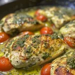 Close-up view of creamy pesto chicken garnished with roasted cherry tomatoes and spinach.