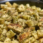 Close-up view of creamy chicken pesto pasta with chicken pieces and vibrant green pesto.