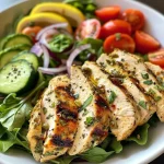 Close-up of a colorful salad featuring grilled lemon herb chicken, mixed greens, cherry tomatoes, cucumber, and red onion.