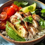 A close-up view of a creamy avocado chicken rice bowl with colorful ingredients.