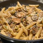A close-up side view of creamy Chicken and Mushroom Pasta with penne noodles.