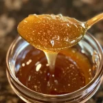 Close-up view of a jar of hot honey with crushed red pepper flakes scattered nearby.