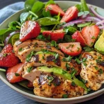 A vibrant salad featuring slices of chicken, strawberries, avocado, and spinach.