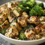 A close-up view of a hearty chicken bowl featuring cubed chicken, broccoli, and brown rice.