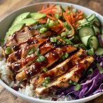 A close-up side view of a BBQ chicken rice bowl featuring juicy grilled chicken atop a bed of rice and colorful vegetables.