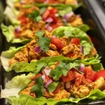 Close-up view of juicy chicken taco lettuce wraps garnished with diced avocado and tomato.