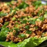 Close-up view of sesame chicken lettuce cups with vibrant green lettuce and garnishes.