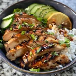 Close-up view of a grilled chicken rice bowl topped with fresh vegetables.
