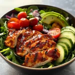 A close-up view of a colorful low carb BBQ chicken bowl featuring sliced chicken, vibrant vegetables, and greens.