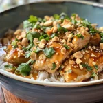 Close-up view of juicy Thai Peanut Chicken garnished with chopped peanuts and cilantro.