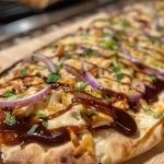 ['Close-up side view of barbecue chicken flatbread topped with cheese and herbs.', 'Juicy barbecue chicken flatbread with melted cheese and red onion slices, presented on a wooden surface.', 'Delicious barbecue chicken flatbread featuring shredded chicken and fresh green onions, seen from the side.', 'Tasty naan flatbread with barbecue chicken, a sprinkle of cheese, and colorful toppings, captured up close.']