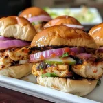 ['Juicy chicken sliders on soft rolls with caramelized onions.', 'Close-up view of chicken sliders garnished with barbecue sauce.', 'Side view of slider rolls filled with grilled chicken and toppings.', 'Delicious chicken sliders stacked on a wooden serving board.']