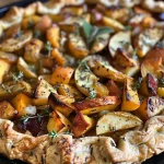 ['Close-up view of a golden-brown Fall Vegetable and Herb Galette filled with root vegetables and herbs.', 'Side perspective of a savory galette with visible apple chunks and root vegetables, on a rustic wooden surface.', 'Detail shot of a baked galette showcasing a flaky crust and colorful filling of vegetables and fresh herbs.', 'A sumptuous Fall Vegetable and Herb Galette with a crispy exterior and vibrant vegetable filling.']