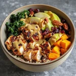 ['Close-up image of a Maple Dijon Fall Harvest Power Bowl featuring colorful ingredients.', 'Side view of a bowl with quinoa, chicken, sweet potato, and vibrant garnishes.', 'Detailed view of a nutritious power bowl with sliced apple and roasted pecans.', 'Delicious bowl filled with baby kale, dried cranberries, and drizzled maple dressing.']