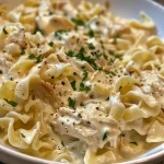 Close-up view of creamy chicken and noodles in a bowl, garnished with parsley.
