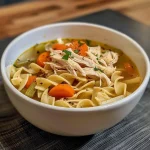 A close-up view of homemade chicken noodle soup with carrots, celery, and egg noodles, served in a bowl.
