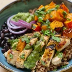 A close-up side view of a roasted chicken bowl with butternut squash, black beans, and guacamole.